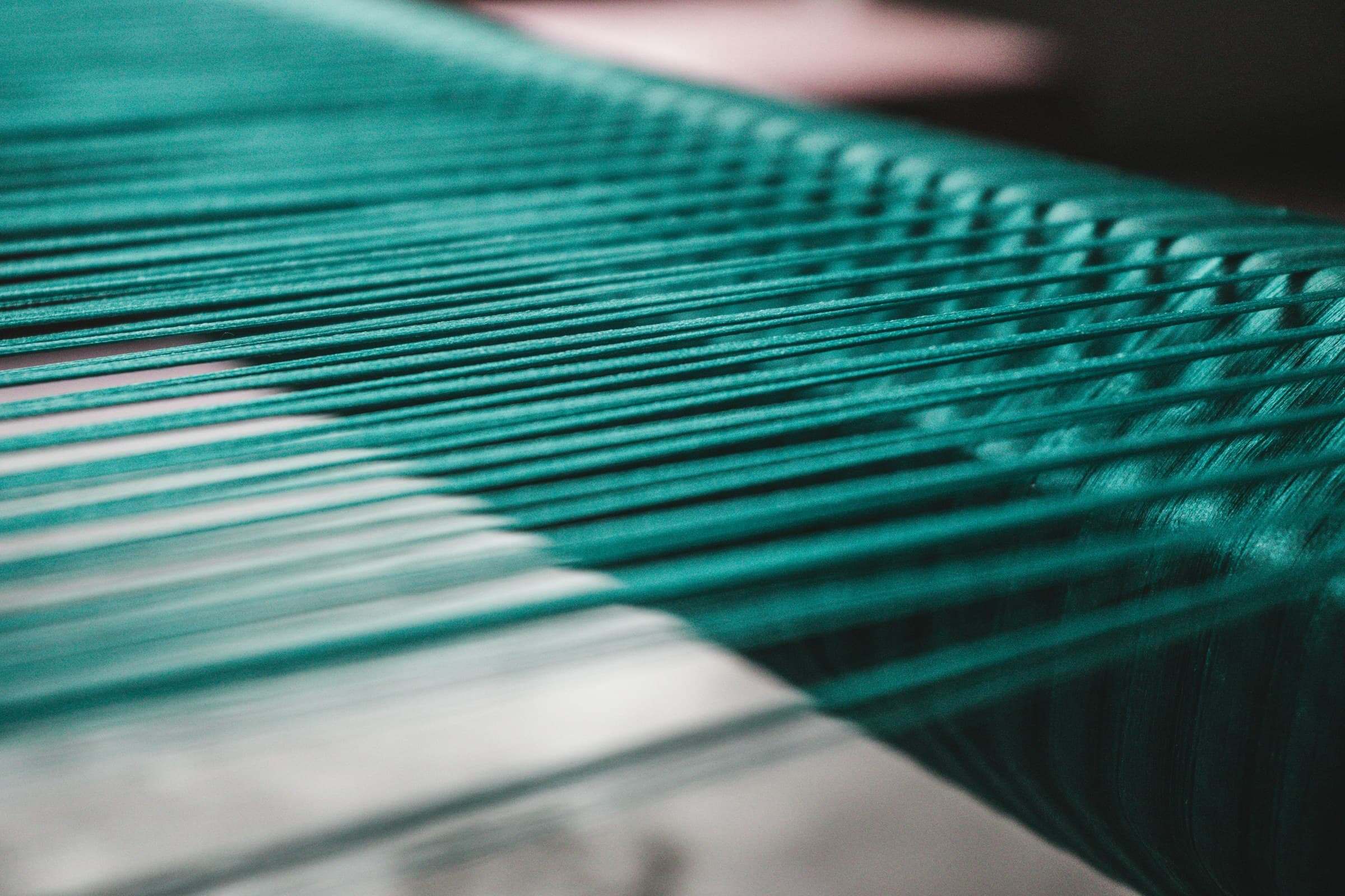 Teal warp threads running across a loom