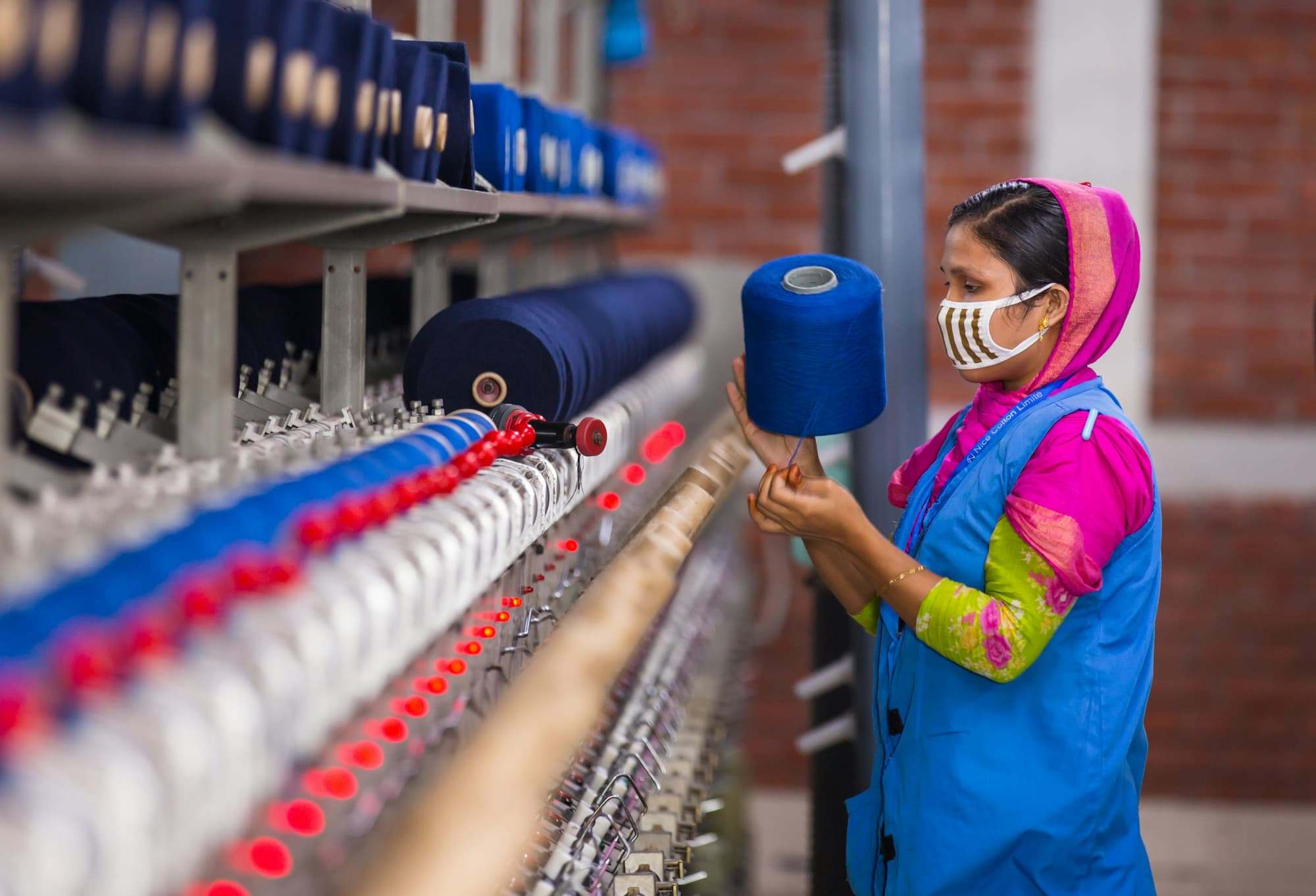 A mill worker handling a cone of blue yarn beside a winding frame